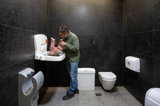 Father Playing With Baby While Changing Diaper In Public Bathroom