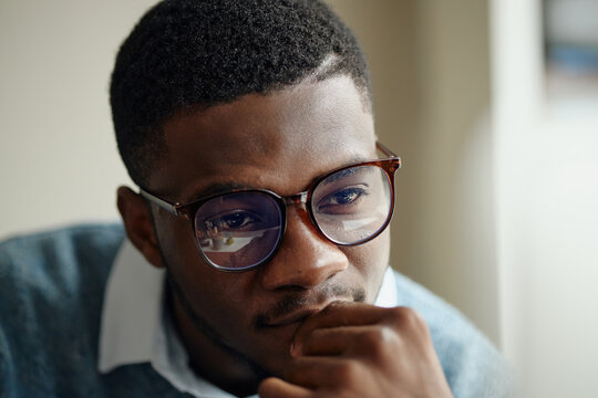 Close up of young Black man wearing eyeglasses, thinking while viewing screen, conveying focus and decision making. Useful for business strategy, office work, productivity