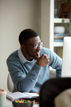 Vertical shot of young Black man working at desktop computer, holding pen and planning ideas at office. Suitable for office work, productivity, business strategy content