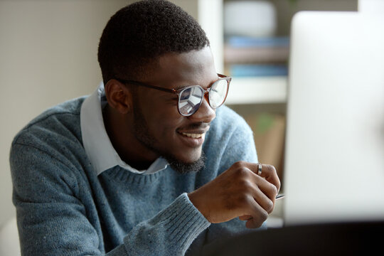 Young African American man working on laptop, smiling while reviewing online content. Ideal for e commerce, office work
