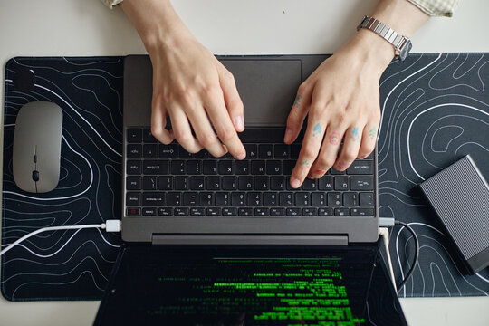 Overhead shot of young adult woman typing on laptop with code on screen, working at desk and managing digital tasks. Suitable for remote work, programming, cybersecurity, tech marketing