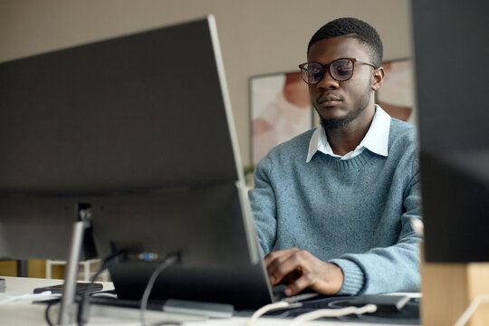 Young adult Black man working at desktop computer in office, typing and focusing on digital tasks and productivity. Useful for business technology, corporate workflow, remote work themes