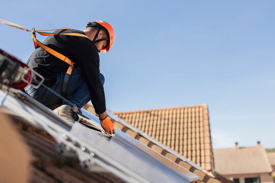 Worker installing solar panels on residential roof with safety harness