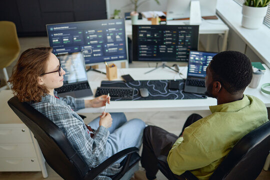 High angle view of Caucasian woman and African American man reviewing analytics dashboards on monitors, collaborating on data strategy. Ideal for business intelligence or teamwork marketing