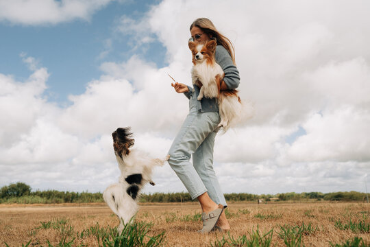 Woman Holding Papillon Dog While Another Dog Jumps Outdoors
