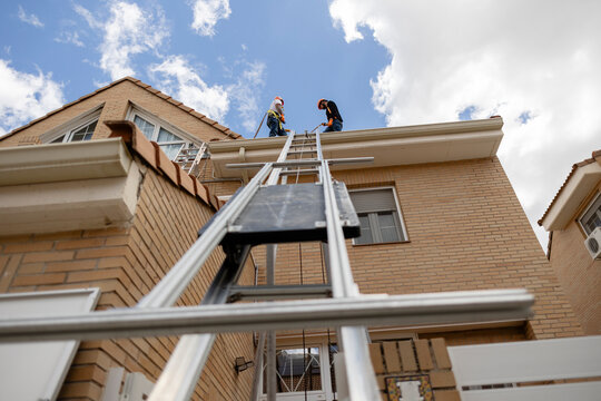 Workers installing new gutter on residential roof structure