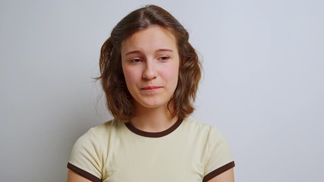 sweet young woman with dental braces smiles subtly, showing a genuine and somewhat shy expression, standing against a neutral studio background