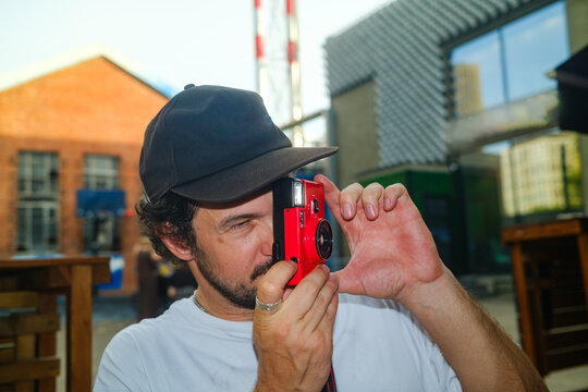 Man Takes Photo With a Red Camera in Urban Setting During Daytime