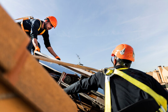 Workers installing solar panels on rooftop with safety equipment