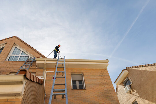 Worker performing roof and gutter cleaning using pressure washer