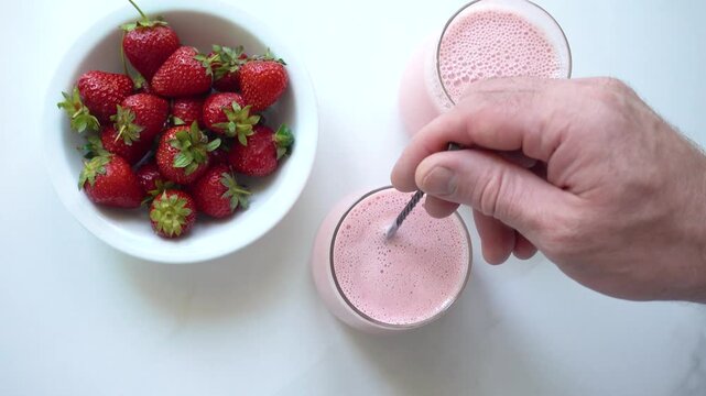 Hands stirring strawberry yogurt in a glass with a spoon. Symbolizes probiotics, healthy eating, and the nutritional value of dairy products. Top view. Ideal for wellness, food, and lifestyle content