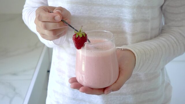 Hands stirring strawberry yogurt in a glass with a spoon. Symbolizes probiotics, healthy eating, and the nutritional value of dairy products. Top view. Ideal for wellness, food, and lifestyle content