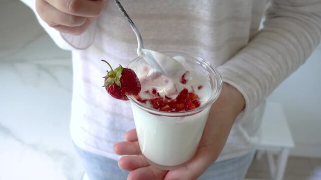 Hands stirring strawberry yogurt in a glass with a spoon. Symbolizes probiotics, healthy eating, and the nutritional value of dairy products. Top view. Ideal for wellness, food, and lifestyle content