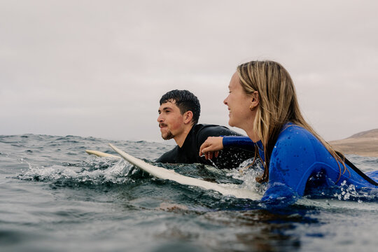 A pair of surfers paddle toward the open sea on their surfboards