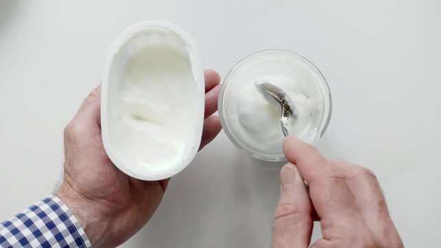 Hands stirring strawberry yogurt in a glass with a spoon. Symbolizes probiotics, healthy eating, and the nutritional value of dairy products. Top view. Ideal for wellness, food, and lifestyle content