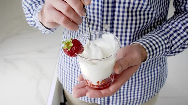 Hands stirring strawberry yogurt in a glass with a spoon. Symbolizes probiotics, healthy eating, and the nutritional value of dairy products. Top view. Ideal for wellness, food, and lifestyle content