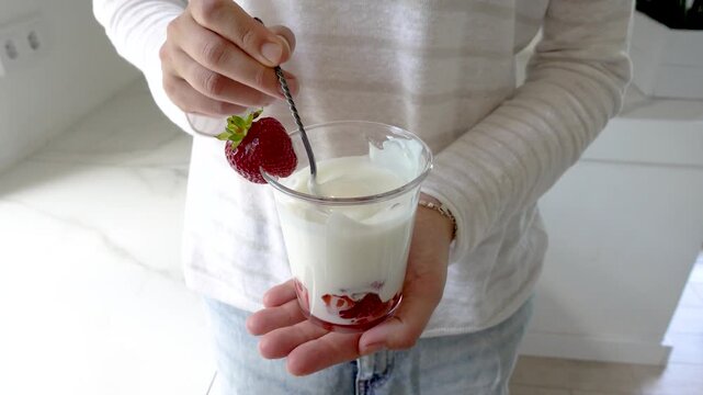 Hands stirring strawberry yogurt in a glass with a spoon. Symbolizes probiotics, healthy eating, and the nutritional value of dairy products. Top view. Ideal for wellness, food, and lifestyle content