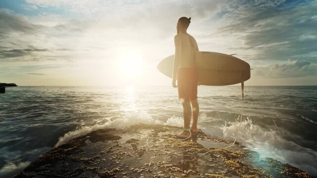 Surfer stands in the ocean, holding a surfboard while gazing at a stunning tropical sunset. Warm golden light illuminates the scene, capturing the essence of adventure, freedom, and connection with