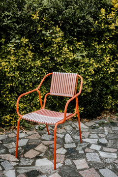 Colorful Chair Stands Alone by Green Hedge on Stone Path