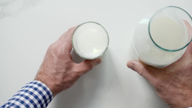 Man's hand pours fresh milk from a glass bottle into a clear glass on a white marble table. Symbolizes dairy nutrition, healthy breakfast, and organic farming. Ideal for food and wellness content