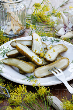 Pickled cucumbers with dill flowers, garlic, and horseradish, cut in half, on a plate, close-up. 