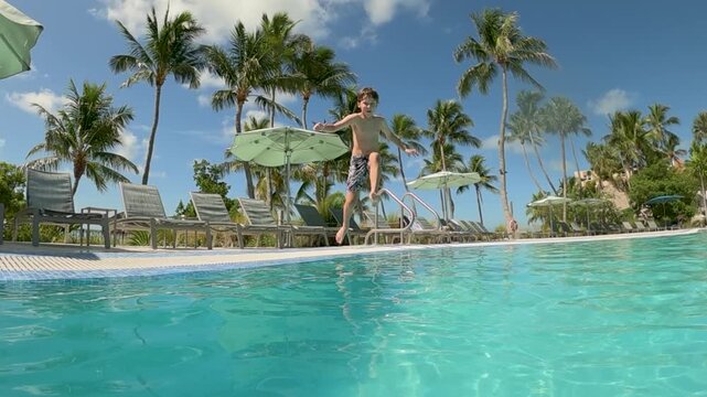Young boy jumping into the pool, extreme slow motion, summer vacation vibes with palm trees