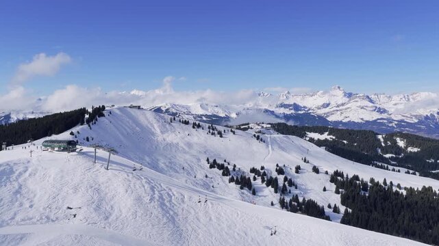 Aerial footage capturing a panoramic view of snow-covered ski slopes and a chairlift station in the Megeve area, with skiers visible on the pistes. The scene features pine forests and expansive