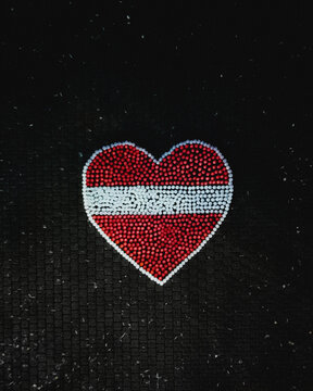 Aerial view of candles arranged in a heart shape with the colors of the Latvian flag on a dark paved surface in Riga, Latvia.