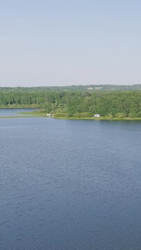 Aerial footage showing the tranquil waters of Lac du Bourdon bordered by lush green forest, with a few campers or caravans parked along the shoreline. The wide lake surface and surrounding woodland