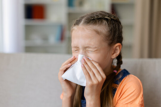 Teen girl blowing her nose with tissue at home, showing cold, flu or allergy symptoms in close portrait for child health, hygiene and seasonal illness concepts
