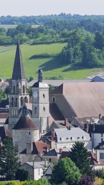 A scenic aerial view of the picturesque village of Vermenton in Burgundy, France, featuring a prominent historic church with a tall spire and clock tower surrounded by traditional houses with tiled