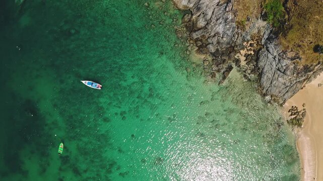 Stunning turquoise water bay and sandy shoreline of Nai Harn Beach in Phuket, Thailand, with small boats anchored near the rocky headland. Summer travel background. Aerial top down view drone shot
