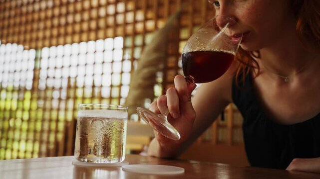 Redhead woman drinking iced coffee from wine glass at cafe