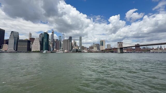 Panoramic, scenic view of Lower Manhattan skyline and Brooklyn Bridge. Motion of cars traffic on FDR drive. Financial district. Motion of East River waves. New York City, United States