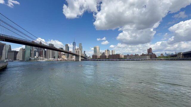 Panoramic, scenic view of Lower Manhattan skyline and Brooklyn Bridge. Motion of cars traffic on FDR drive. Financial district. Motion of East River waves. New York City, United States
