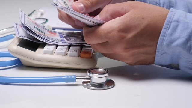 Hands counting us dollar banknotes on a calculator, symbolizing the high cost of healthcare, medical debt, health insurance premiums, and financial planning in the medical field