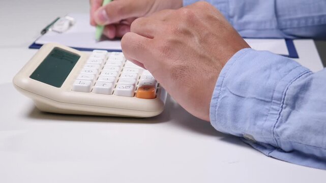 Person working on a budget. Using a calculator to manage finances and make calculations. While simultaneously writing down figures on a clipboard