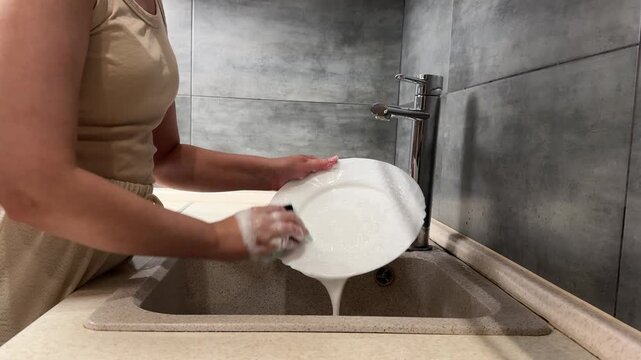  kitchen cleaning scene showing person scrubbing white plate over sink with sponge