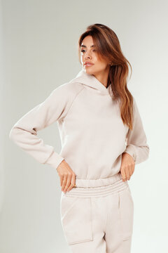 Portrait of a confident young woman wearing a trendy tracksuit posing in a minimalist studio against a white background. 