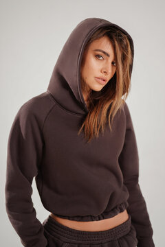 Portrait of a confident young woman wearing a trendy brown tracksuit  standing in a minimalist studio. Modern casual streetwear, athleisure fashion, comfortable outfit