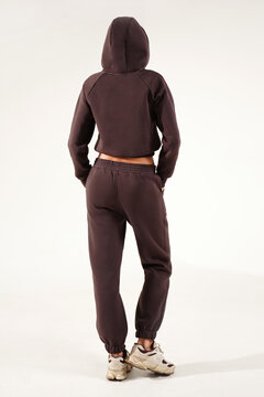 Fashionable young woman wearing a trendy tracksuit  standing in a minimalist studio. Modern casual streetwear, athleisure fashion, comfortable outfit, urban style