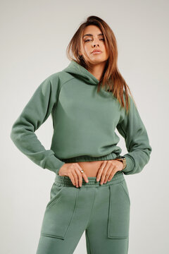 Portrait of a confident young woman wearing a trendy tracksuit  standing in a minimalist studio. Modern casual streetwear, athleisure fashion, comfortable outfit, urban style