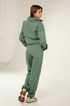 Fashionable young woman wearing a trendy tracksuit  standing in a minimalist studio. Modern casual streetwear, athleisure fashion, comfortable outfit, urban style