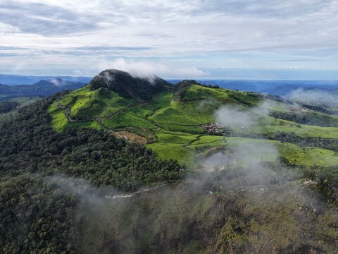 Aerial view of lush green tea plantations and rolling hills surrounding the Parkiran Bawah Kawah Putih Ciwidey area with a small lake in Kecamatan Ciwidey, Jawa Barat, Indonesia.