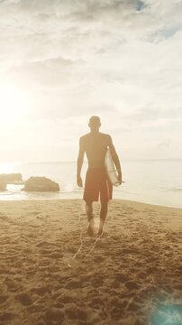 Surfer walking along the sandy beach at sunset, carrying a surfboard while wearing vibrant red shorts. Displaying determination and strength with a prosthetic leg, embracing the beauty of the ocean