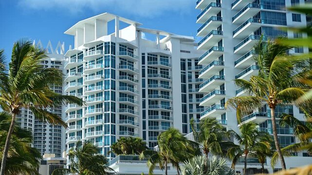Modern glass condominium towers framed by palms, Miami Beach, Florida. Close view of blue tinted facades, white balconies and swaying coconut trees.