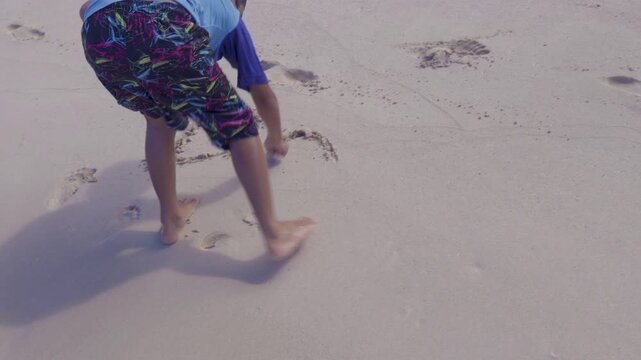 Boy drawing writing word text "DAD" in the sand sea shore with finger for Fathers Day on tropical summer sunny day at Hawaii ocean beach