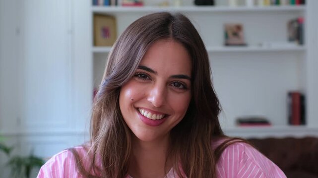 Charming brunette woman engaging in a pleasant video chat, looking directly at the camera with a genuine smile. Her joyful expression conveys happiness and connection during remote communication