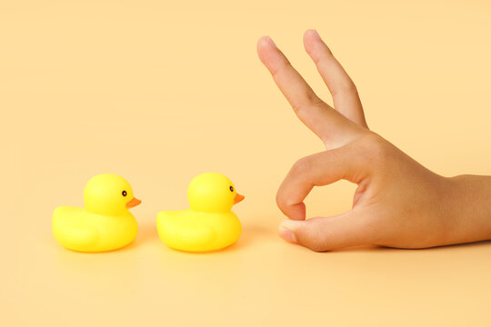 Hand making a flick gesture toward two yellow rubber ducks on a pastel background. Concept of selection, decision making, influence, comparison and human interaction.