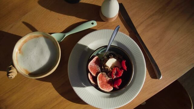 Aesthetic breakfast table with coffee latte and fruit bowl, healthy morning meal with figs and raspberries, sunny brunch flat lay on wooden table